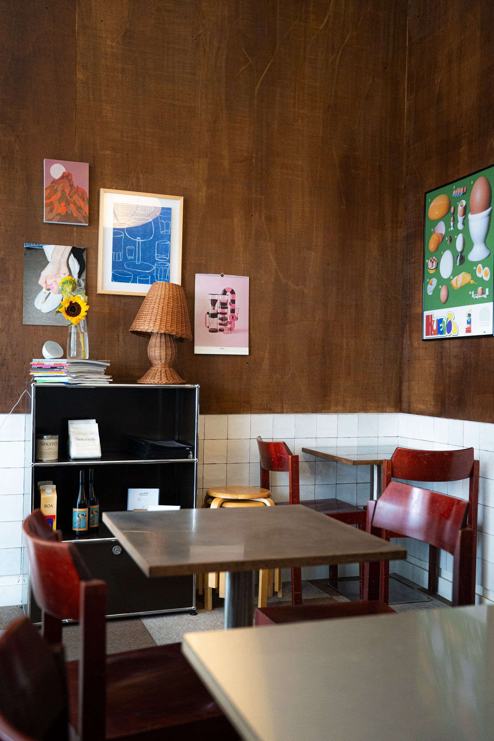 Eine Ecke des Cafes mit holzvertäfelten Wänden, roten Stühlen und einer Sonnenblume auf dem Regal