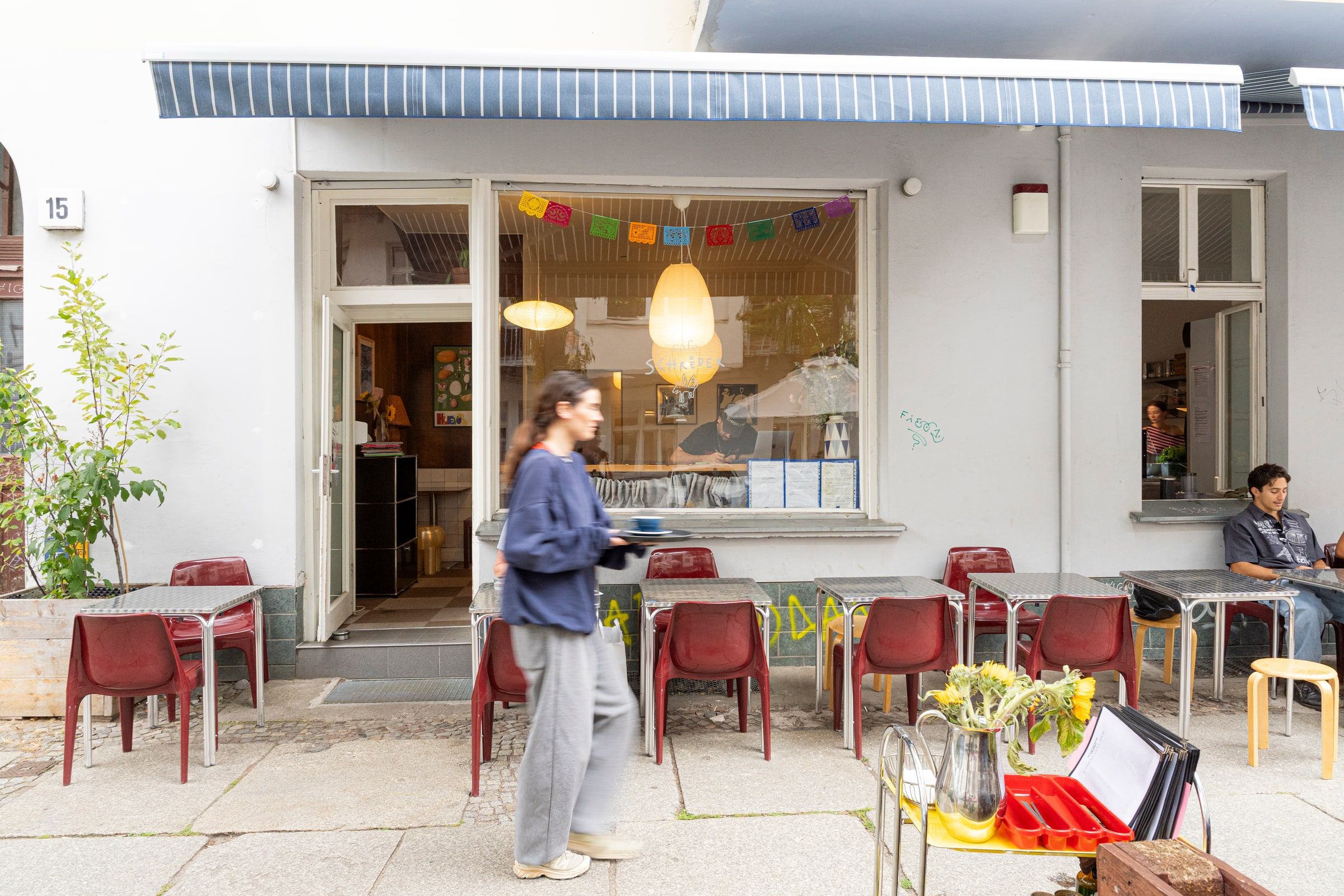 Die Vorderseite des Cafes, mit roten Stühlen auf dem Gehweg unter einer gestreiften Markise