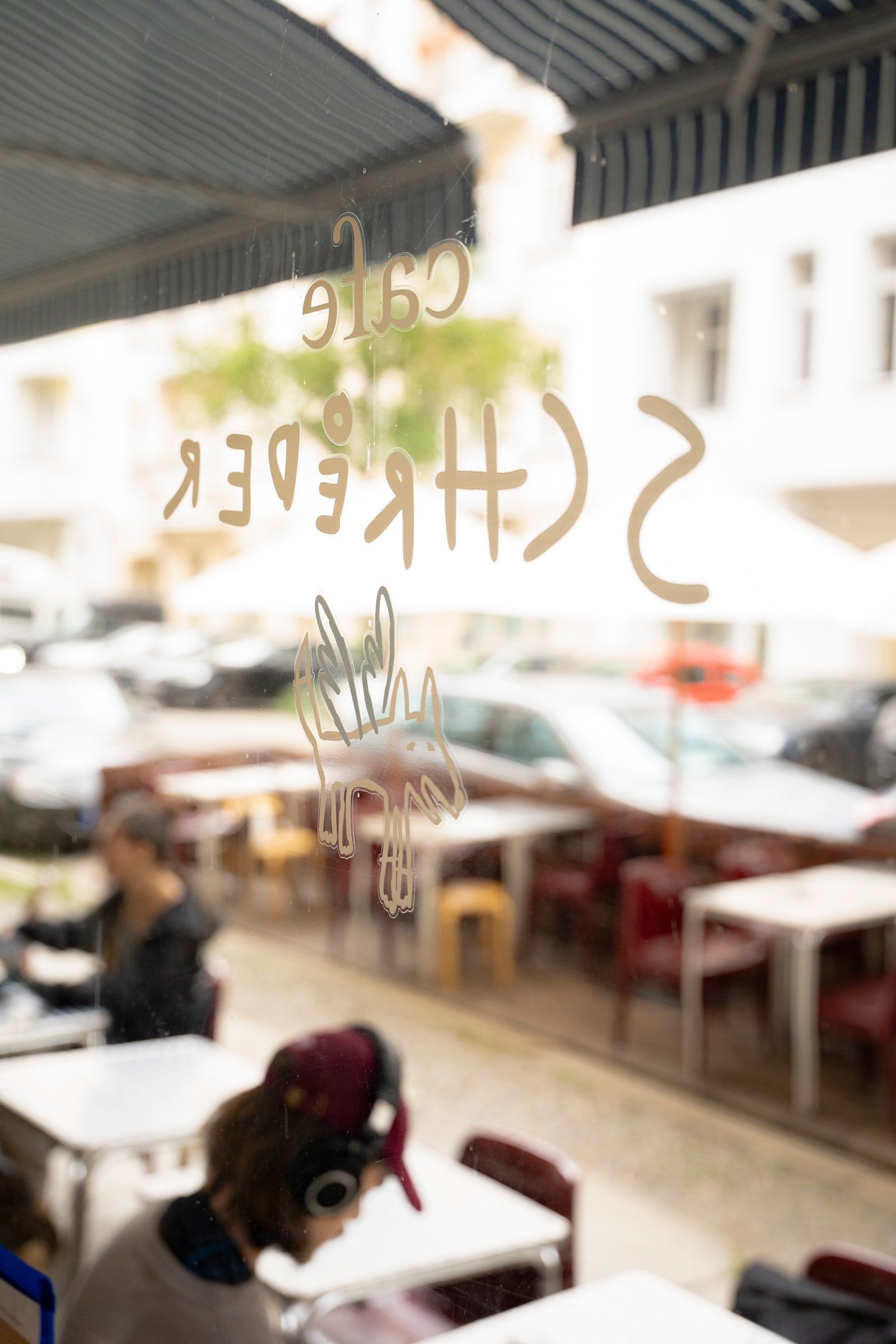 Der Schriftzug von Cafe Schroeder und der gezeichnete Hund auf der Fensterscheibe, mit Blick auf die Terrasse