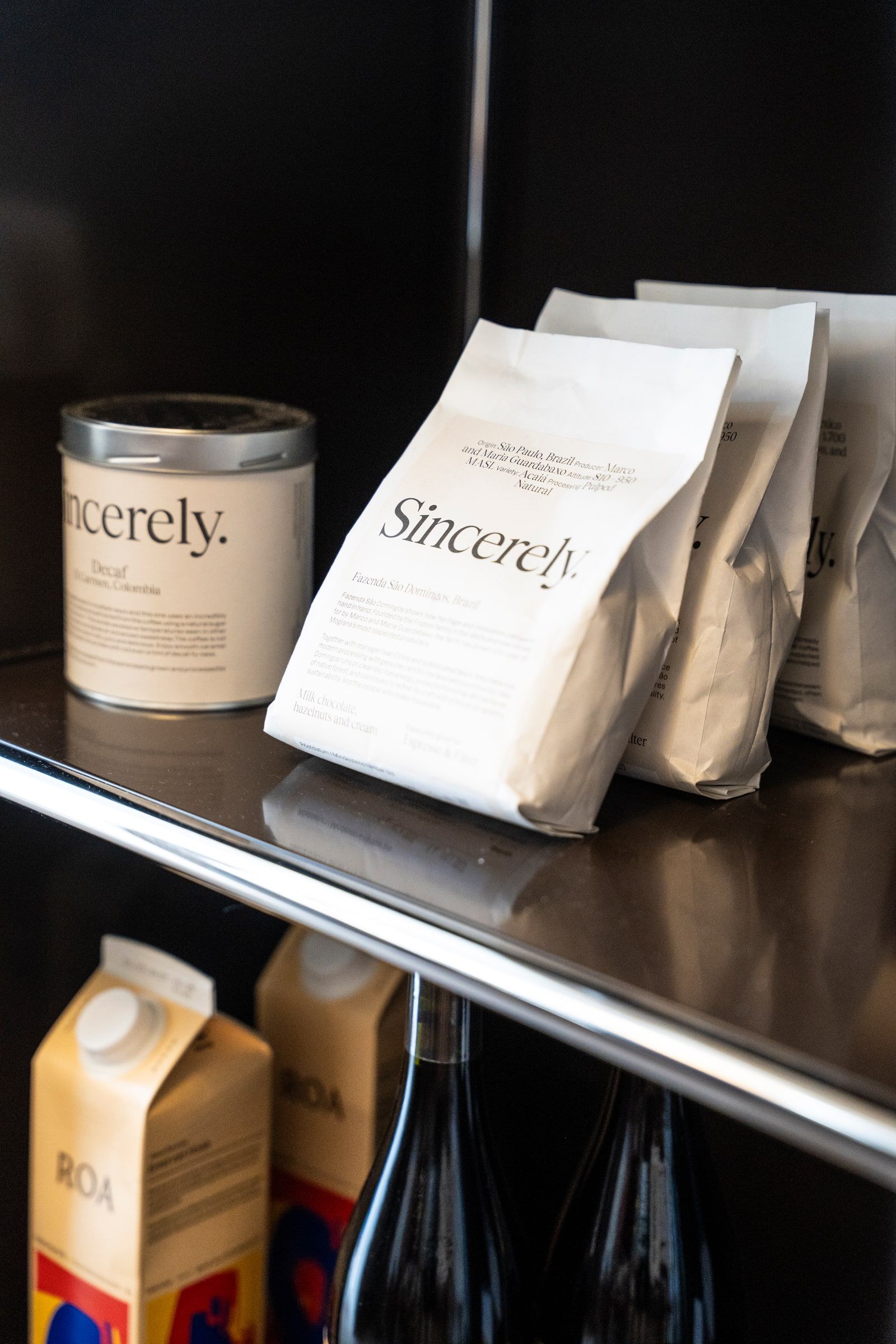Tüten und eine Dose Sincerely-Kaffee auf einem Regal, darunter Kartons und Flaschen